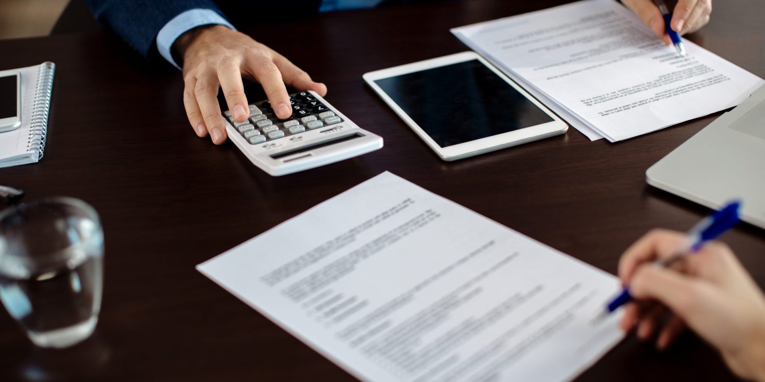 Close-up of real estate agent calculating costs of a mortgage agreement while having a meeting with a client in the office.